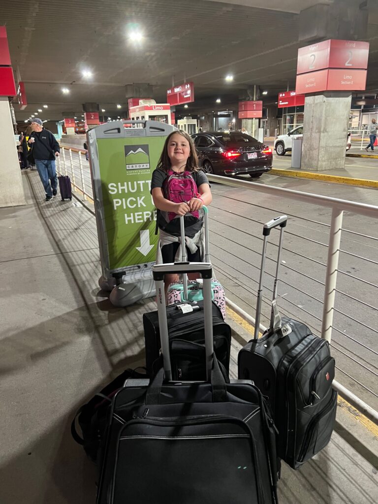 Cassidy standing with 4 bags for just the 3 of us at the Boston airport.